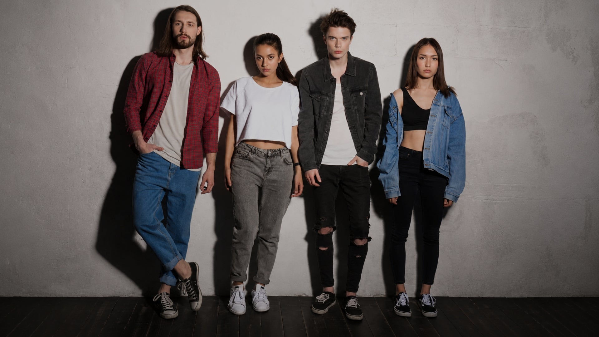 four diverse fashion models posing together against a plain grey wall